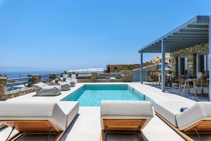 Una piscina en la azotea con sillones de descanso, un muro de piedra y vistas al mar.