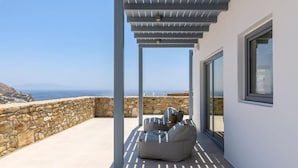 A modern outdoor seating area with a stone wall and a view of the sea.