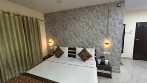 A hotel room with a large bed, two bedside tables, a nightstand, a wall-mounted light, and a door. - 45-room hotel in delightful Varanasi with WiFi, AC. Unwind in comfort (Varanasi)