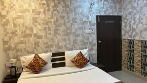 A hotel room with a bed, two decorative pillows, a nightstand with a kettle, and a door with a lock. - 45-room hotel in delightful Varanasi with WiFi, AC. Unwind in comfort (Varanasi)