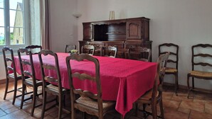 A dining room with a rectangular table covered in a red tablecloth, surrounded by wooden chairs with cushioned seats. - Charming house in the Charolais countryside overlooking the valley (VIRY)