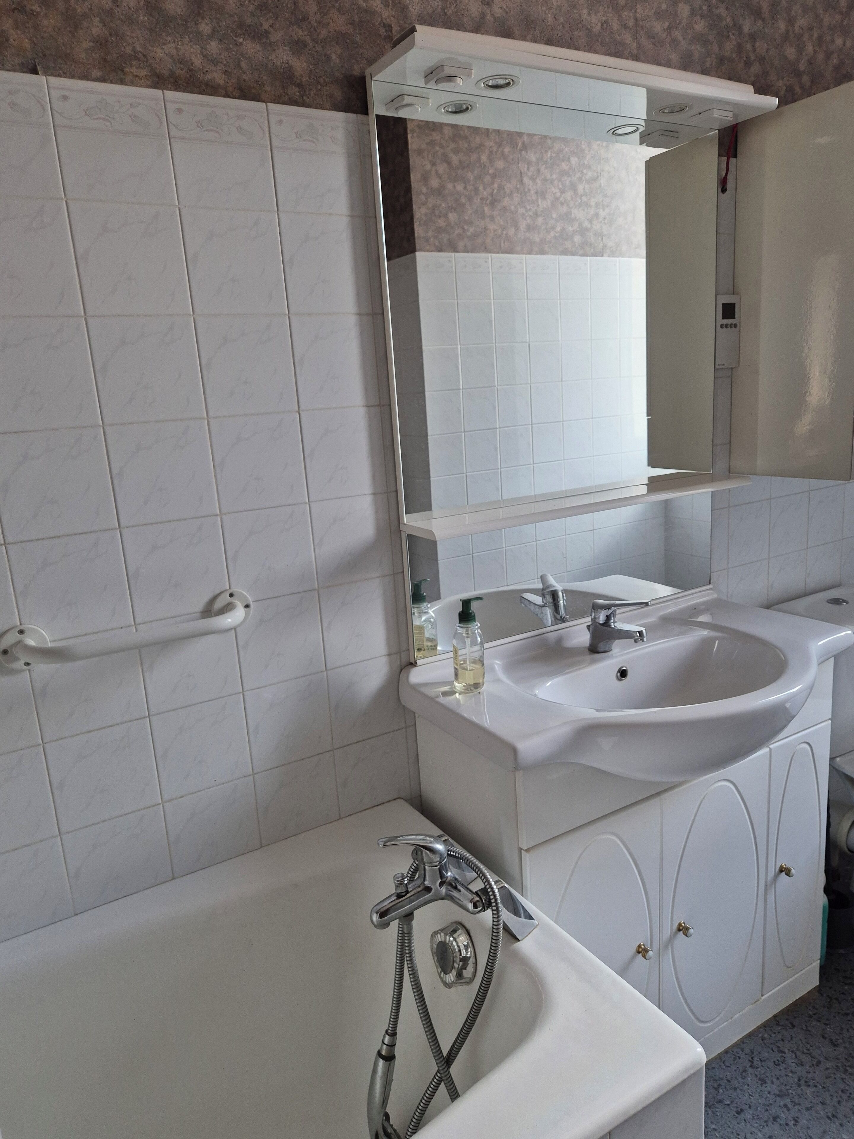 A bathroom with a white sink, mirror, and bathtub. There is a towel rack and a soap dispenser on the sink.