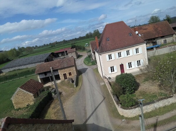 A rural house with a red roof, a stone foundation, and a paved driveway.