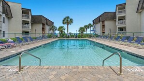 A swimming pool with lounge chairs and palm trees, surrounded by buildings with balconies.