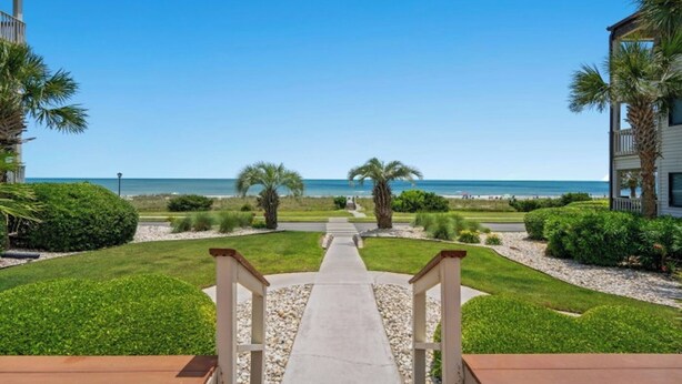 A pathway leading to a beach with a clear view of the ocean, surrounded by well-maintained greenery and palm trees.