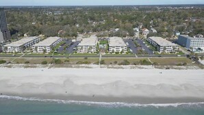A beachfront hotel with multiple buildings, a parking lot, and a sandy beach.