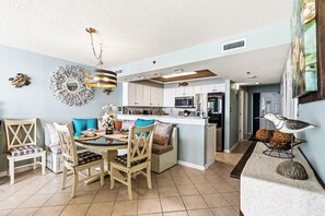 A modern kitchen with white cabinets, a central island, and a dining area with wooden chairs and a glass table. - Oceanfront 3BR -Paradise Pointe 8B- I/O Pools (North Myrtle Beach)