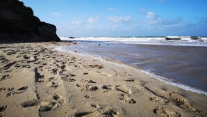 Une plage de sable avec des empreintes, des vagues et une falaise.