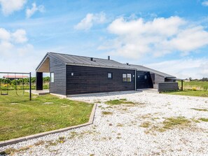 A modern building with a sloped roof, a gravel driveway, and a grassy area with a swing set.