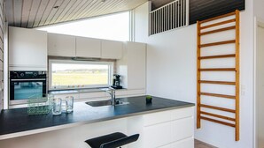 Une cuisine moderne dotée d’un grand îlot central, d’un four encastré et d’une fenêtre donnant sur un champ.