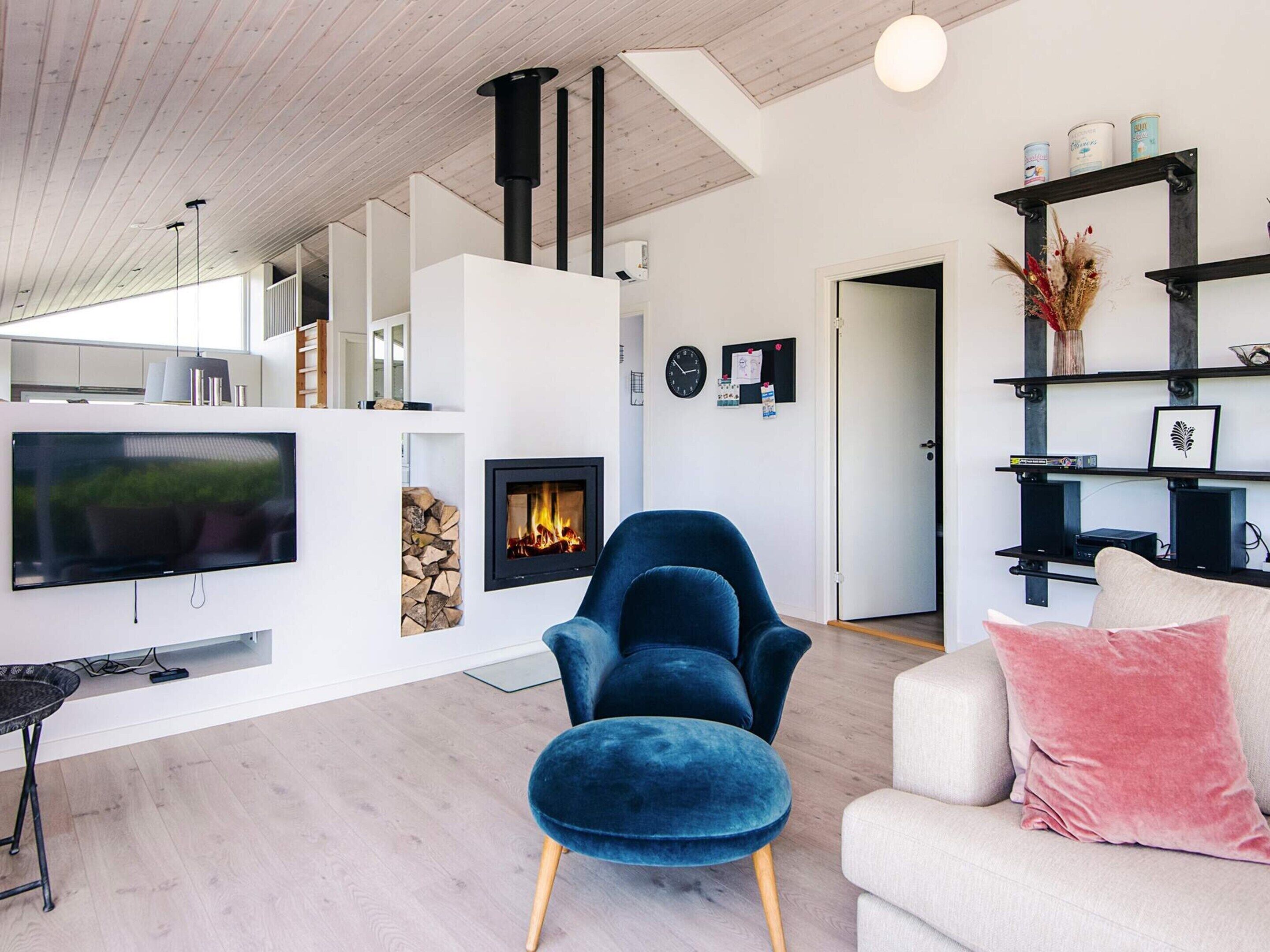 A modern living room with a fireplace, a large flat-screen TV, and a blue armchair.