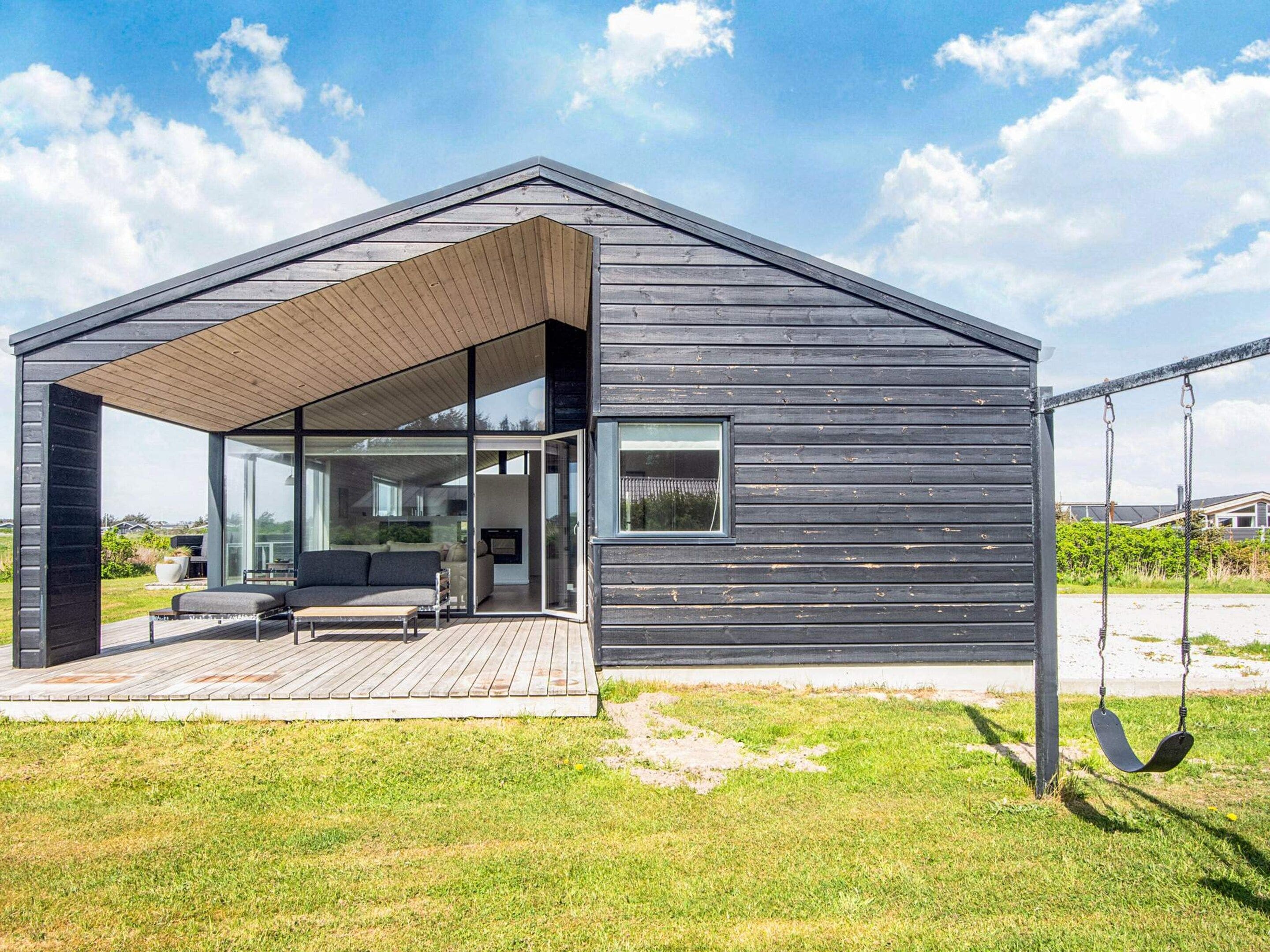 A modern house with a covered patio, a swing set, and a view of the surrounding landscape.