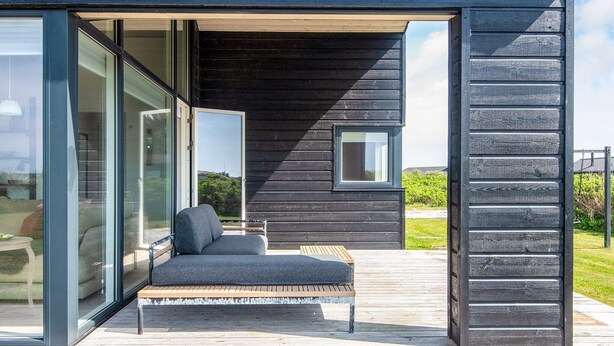 Une maison moderne avec une porte vitrée donnant sur une terrasse aménagée avec un banc et une petite table.