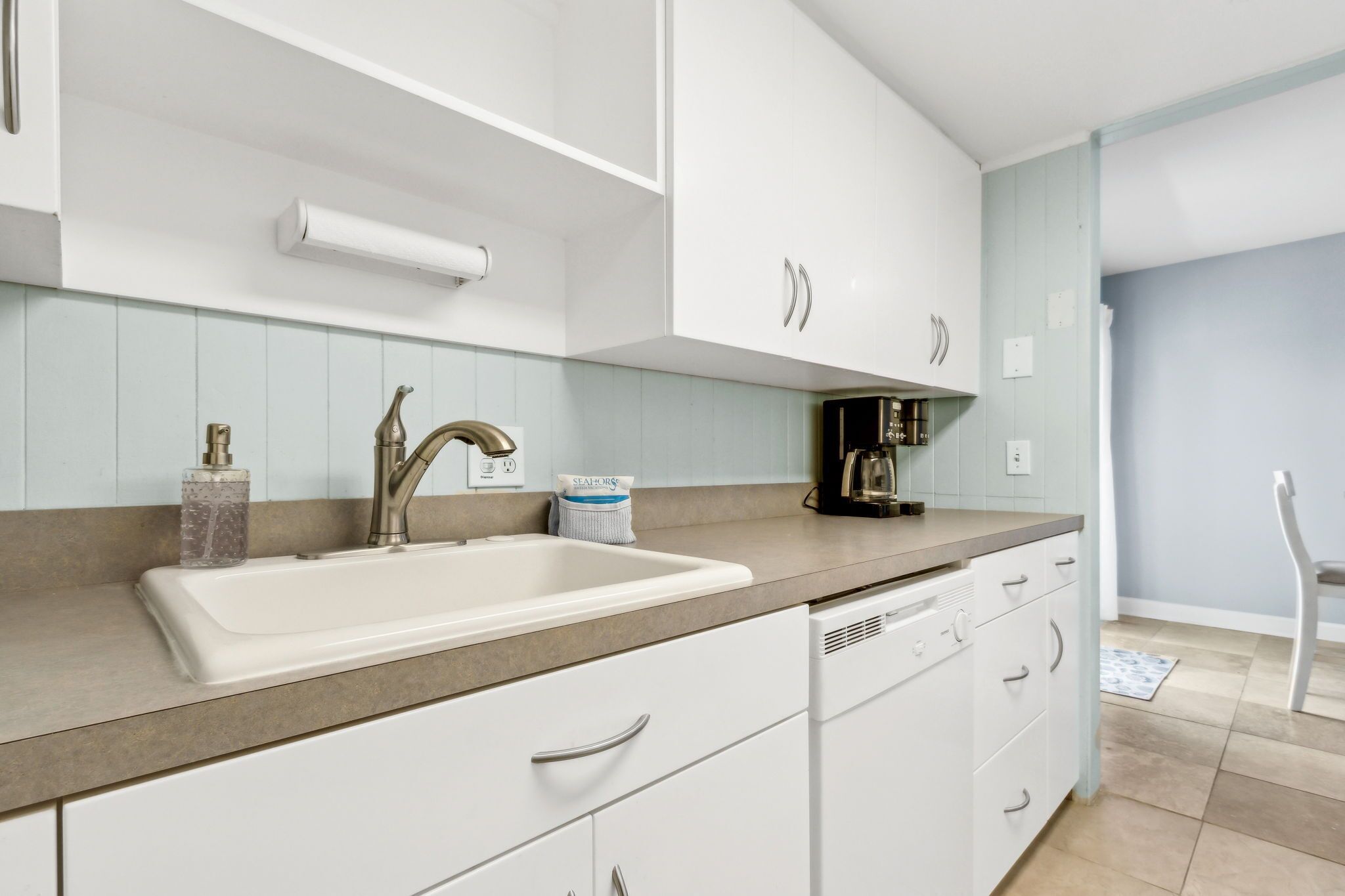 A modern kitchen with white cabinets, a sink, and a coffee maker.