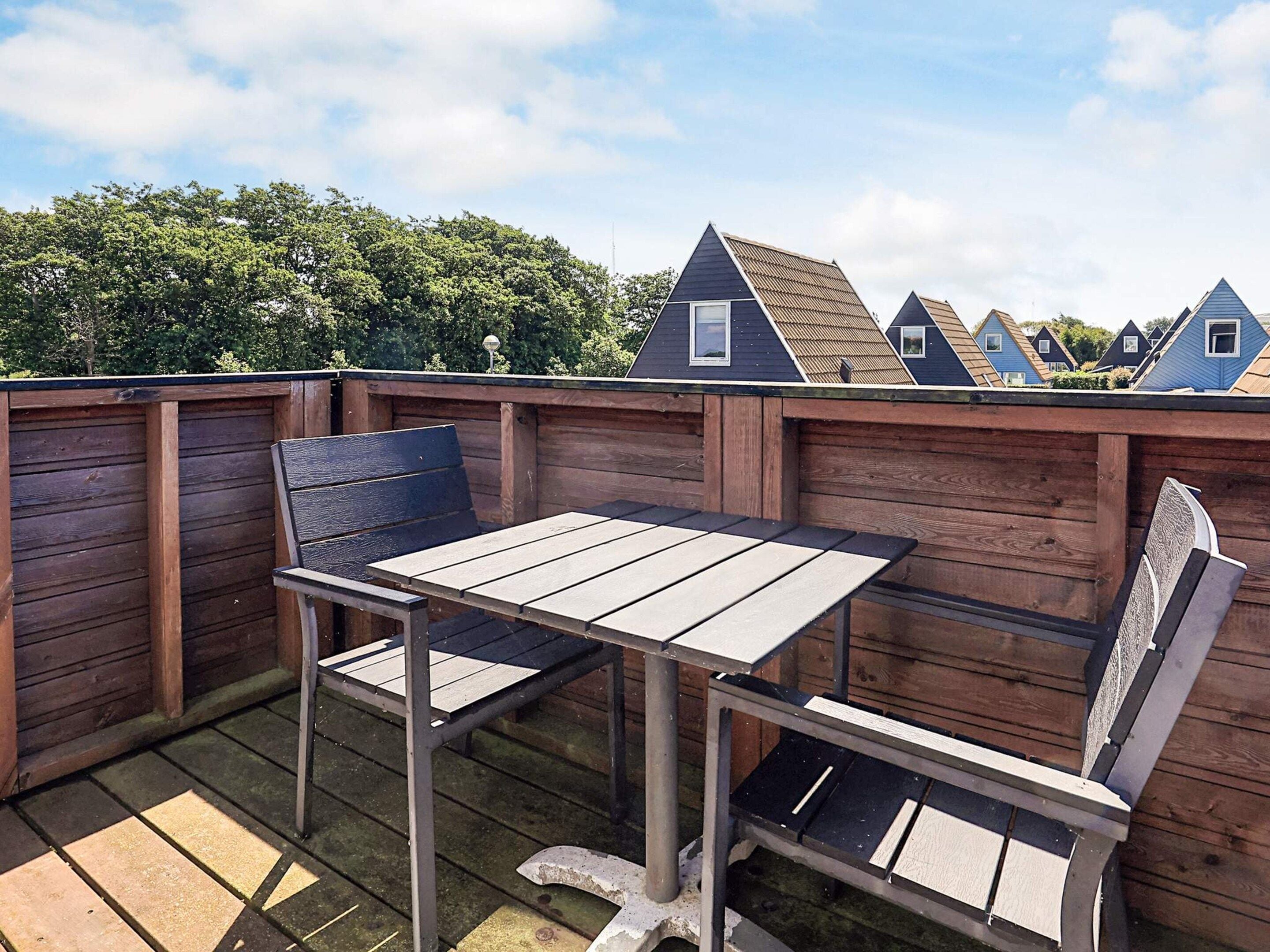 A wooden deck with a metal table and bench, surrounded by a wooden fence.