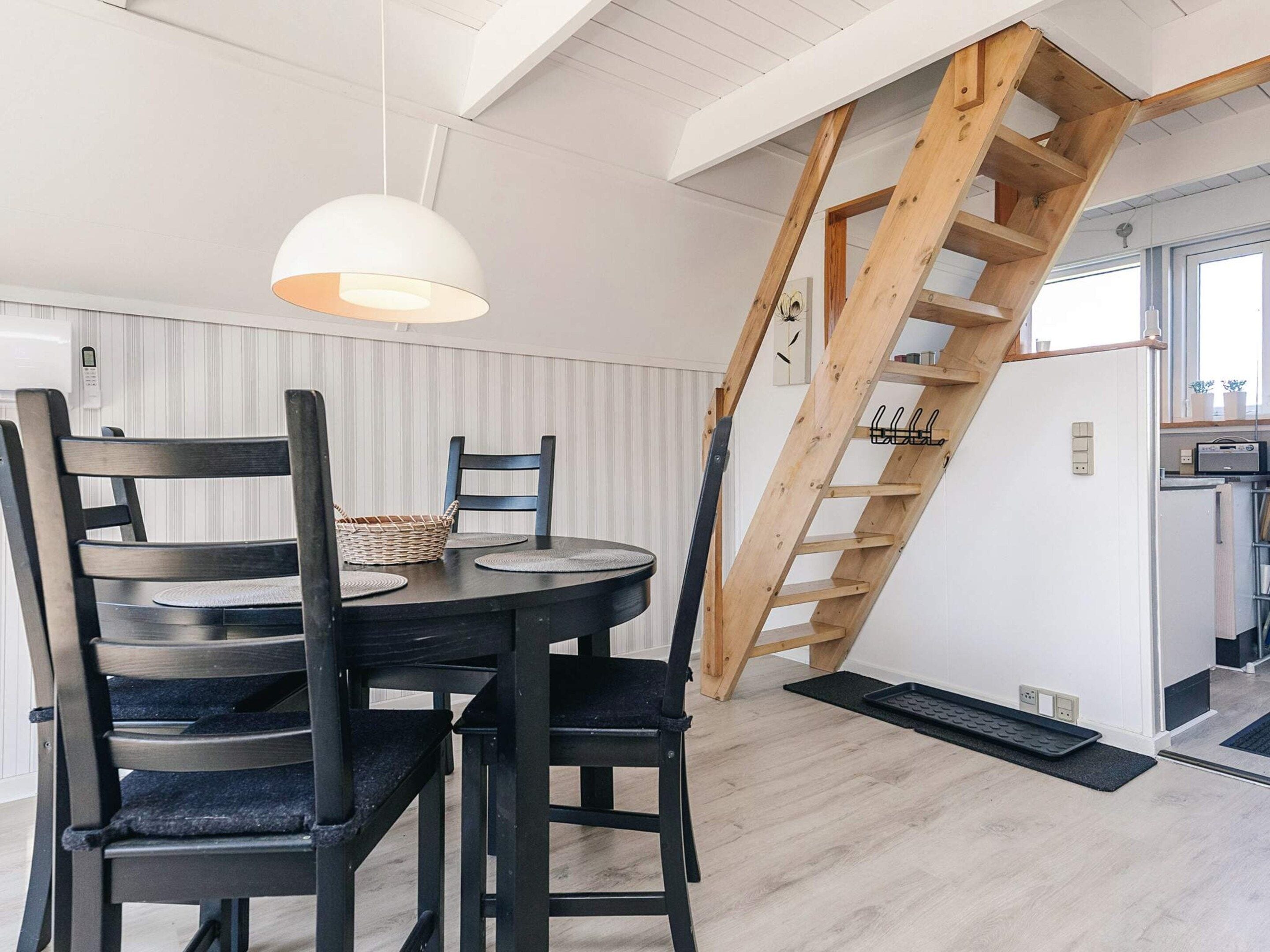 Een eetruimte met een ronde tafel, stoelen, een hanglamp en een houten trap.