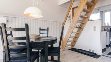 Een eetruimte met een ronde tafel, stoelen, een hanglamp en een houten trap.