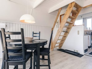 A dining area with a round table, chairs, a hanging light fixture, and a wooden staircase.
