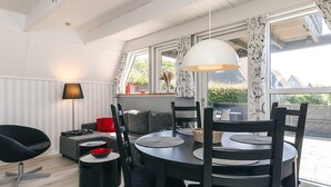 Ein modernes Wohnzimmer mit einem runden Esstisch, schwarzen Stühlen, einem schwarzen Sofa, einem roten Kissen, einer Stehlampe und großen Fenstern mit Vorhängen.