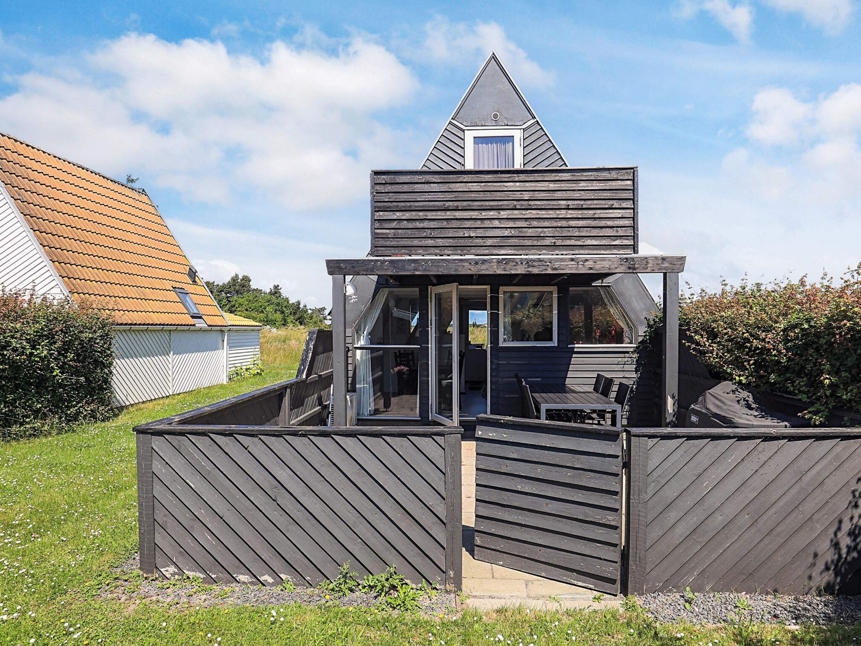 A modern, compact wooden structure with a sloped roof, a balcony, and a small enclosed porch area.