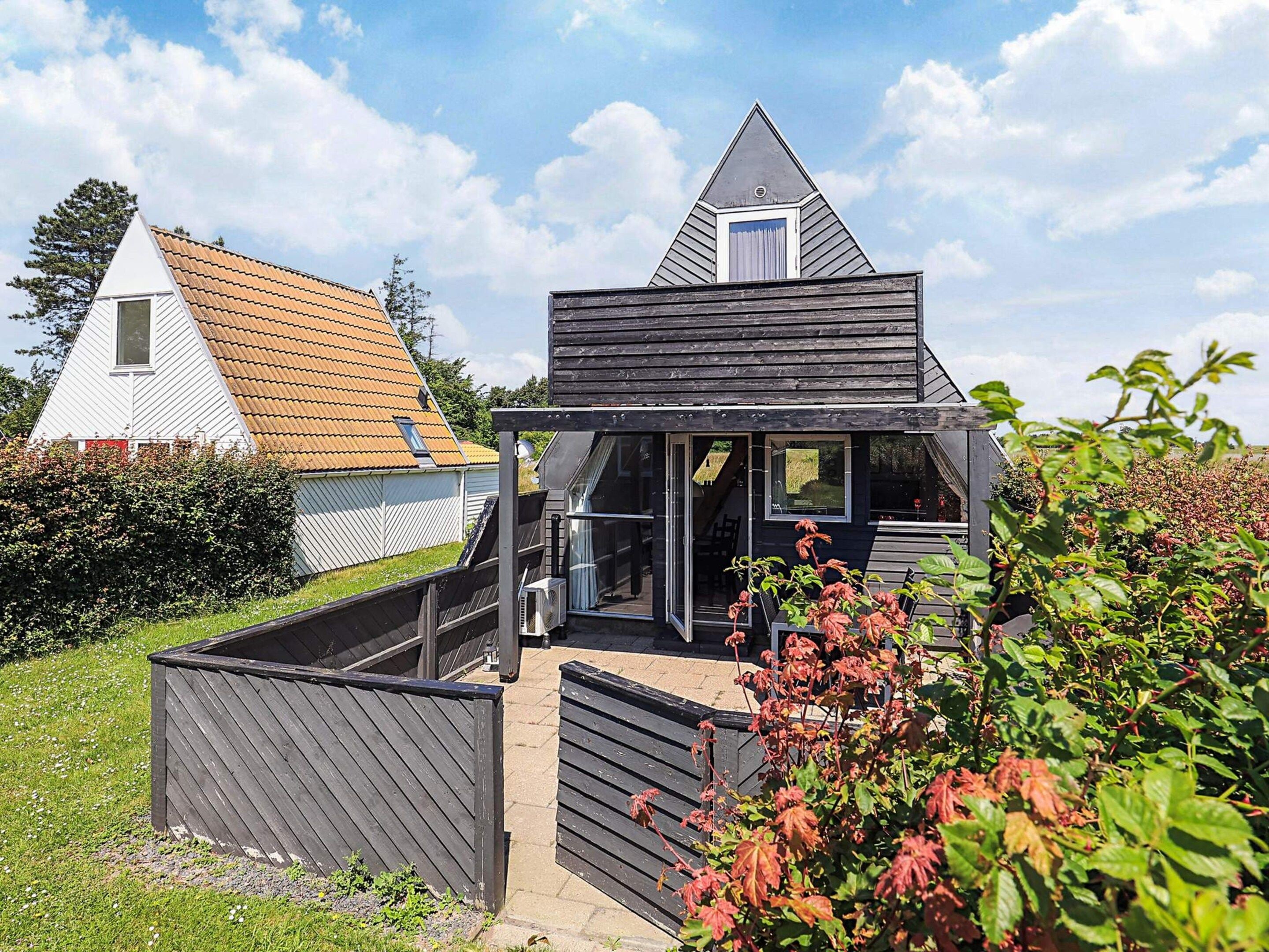 A modern two-story house with a sloped roof, a balcony, and a small attached shed.