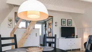 Ein Essbereich mit einem schwarzen Tisch, grauen Platzsets, einem gewebten Korb und einer weißen Decke mit Holzbalken.