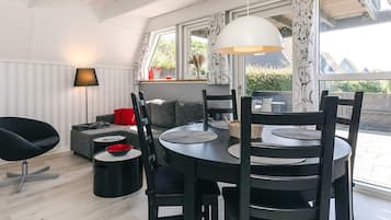 Een moderne woonkamer met een ronde eettafel, zwarte stoelen, een zwarte bank, een rode kussen, een vloerlamp en een groot raam met gordijnen.