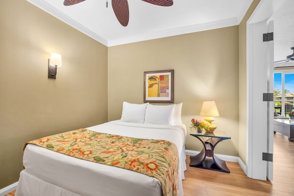 A hotel room with a bed, a wall-mounted lamp, a framed picture, a side table with a lamp, and a ceiling fan.