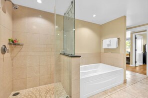 A modern bathroom with a glass-enclosed shower, a white bathtub, and a shelf with toiletries.