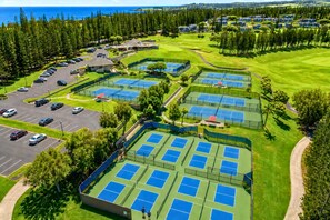 Vista aérea de un campo de golf con múltiples canchas de tenis, un estacionamiento y follaje circundante.
