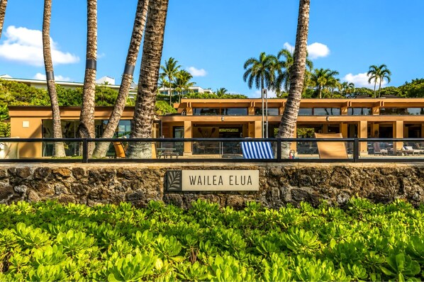 A hotel with a stone wall, palm trees, and a sign reading 'WAILEA ELUA'.