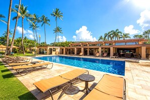 A pool area with lounge chairs and tables, surrounded by palm trees and a modern building structure. - Wailea Elua | Ocean View 4 BR, Sleeps 12 | Car Incl. w/ 6+ Nights | WEV ML-1137 by KBM (Wailea)