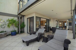 A modern outdoor patio with wicker furniture, a potted plant, and a glass door leading to an interior space.