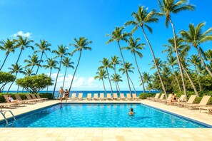 A poolside area with lounge chairs and palm trees, overlooking a clear blue sky.
