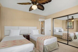 A hotel room with two beds, a ceiling fan, a large mirror, and a door leading to a bathroom.