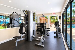 A gym with various exercise machines, a clock, and a view of a pool and palm trees through large windows. - Wailea Elua | Ocean View 4 BR, Sleeps 12 | Car Incl. w/ 6+ Nights | WEV ML-1137 by KBM (Wailea)