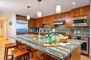 A modern kitchen with granite countertops, stainless steel appliances, wooden cabinets, and bar stools.