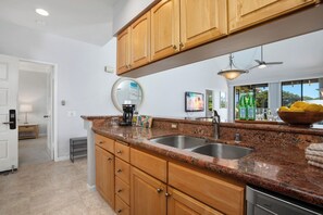 A kitchen with wooden cabinets, granite countertops, a double sink, a coffee maker, and a bowl of lemons. - Grand Champions | Ocean View 5 BR, Sleeps 12 | Car Incl. w/ 6+ Nights | GCH ML-1149 by KBM (Wailea)