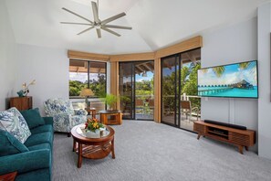A spacious living area with a ceiling fan, a large flat-screen TV, a sofa, a coffee table, and a balcony with a view of the ocean. - Grand Champions | Ocean View 5 BR, Sleeps 12 | Car Incl. w/ 6+ Nights | GCH ML-1149 by KBM (Wailea)