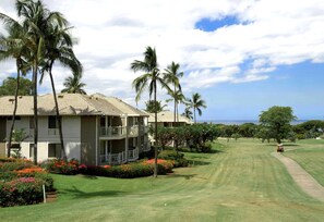 A two-story building with a balcony, surrounded by palm trees and a well-maintained lawn. - Grand Champions | Ocean View 5 BR, Sleeps 12 | Car Incl. w/ 6+ Nights | GCH ML-1149 by KBM (Wailea)