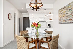 A modern kitchen with white cabinets, a glass dining table, wicker chairs, and a decorative fish painting.