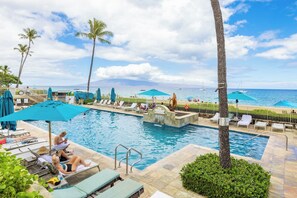 A pool area with lounge chairs, umbrellas, and a view of the ocean.
