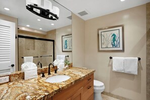 A bathroom with a granite countertop, a sink, a mirror, a towel rack, and a toilet.