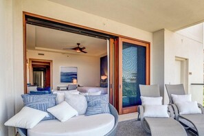 Un balcon avec un canapé et des fauteuils, un ventilateur de plafond et une vue sur l’intérieur.