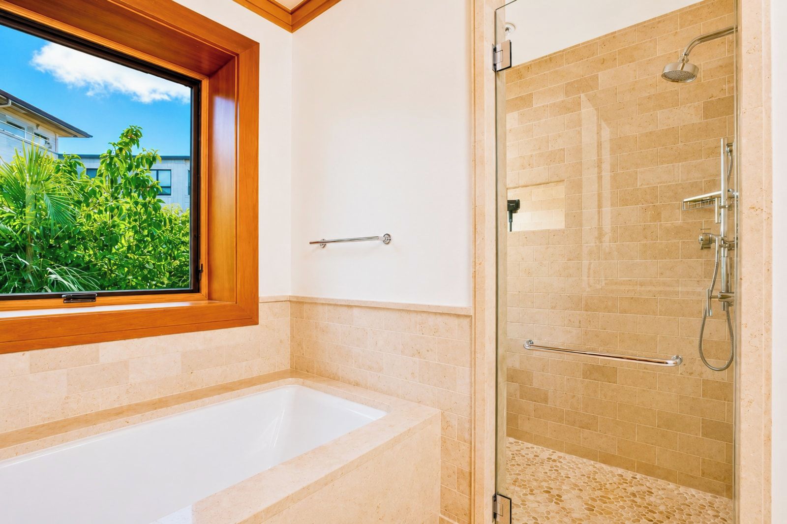 A bathroom with a bathtub, a glass shower enclosure, and a window with a view of greenery.