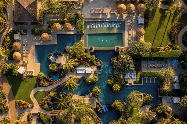 An aerial view of a resort with a central swimming pool, multiple lounge areas, and lush landscaping.