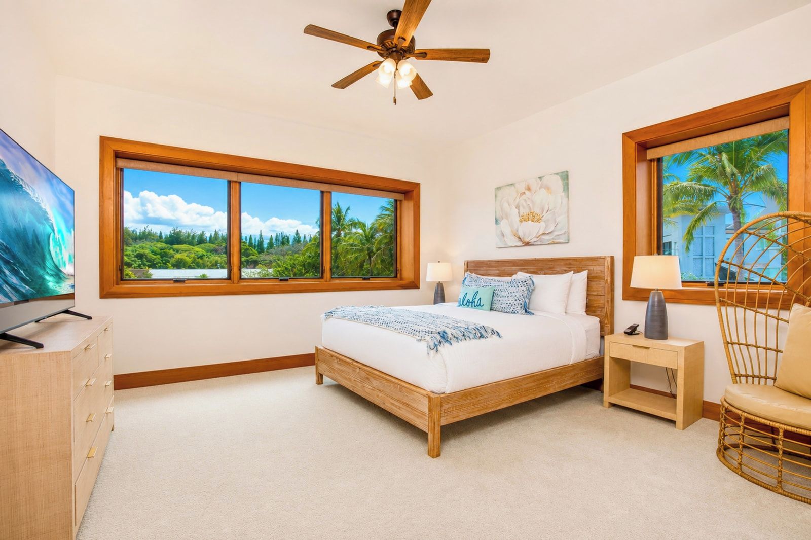 A bedroom with a bed, a TV, a window with a view, a ceiling fan, and a chair.