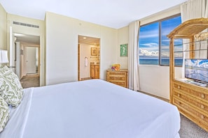 Une chambre d’hôtel avec un grand lit, une commode en bois, une télévision et une vue sur l’océan.