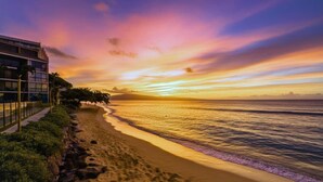 Une plage au coucher du soleil, un bâtiment doté d’un balcon et un ciel dégagé.