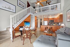 A spacious living area with a dining set, a grey sofa, and a kitchen with wooden cabinets. - Papakea | Ocean View 6 BR, Sleeps 16 | Car Incl. w/ 6+ Nights | PKC ML-1169 by KBM (Lahaina)